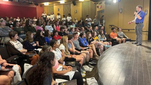 Students in a large lecture hall listen intently to a speaker on the stage.